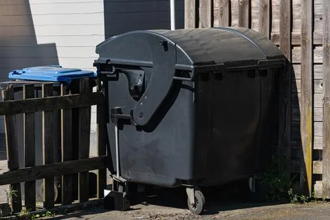 Large black garbage bin next to wooden fence in a quiet area 스톡 사진