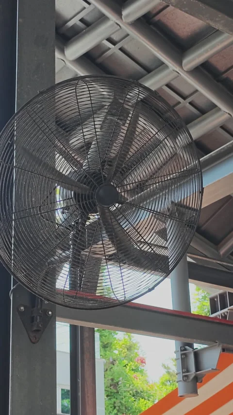 Large black industrial fan mounted on a wall column, its blades spinning Stock Footage 346185280