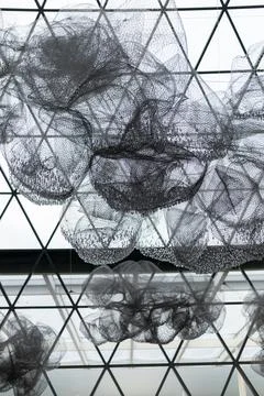 Large black mesh structures float under a geometric ceiling in an airy space. Foto stock