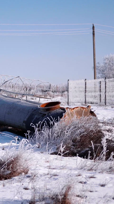 Large black pipe lying on snowy ground with orange cap and frozen grass Stock Footage 347360419