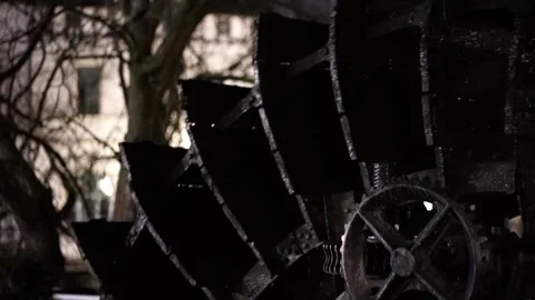 A large black water wheel is in the foreground of a dark background Stock Footage 296101689