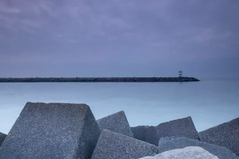 Large blocks of grey stone with a lighthouse in the distance, at dusk Stock Photos