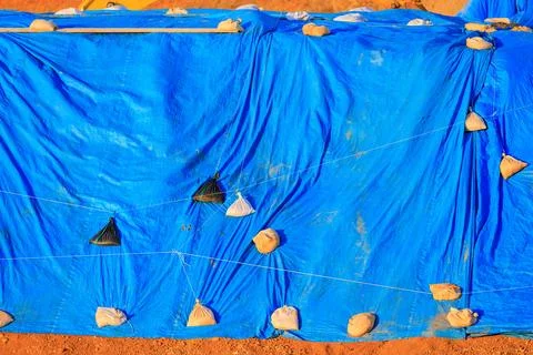 Large blue tarp held down by sandbags covers materials outdoors Foto stock