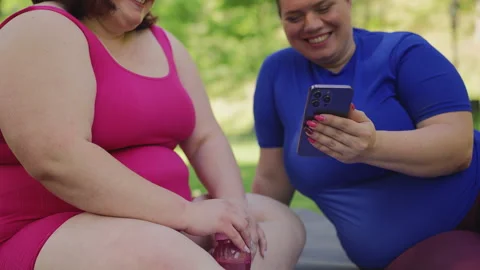 Large-bodied sisters using a calorie calculator app on phone after training Stock Footage 333634000