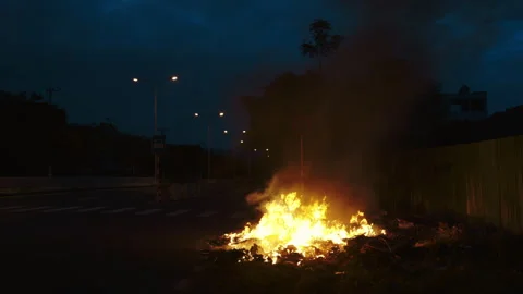 Large bonfire of unauthorized waste burns on roadside edge at night Stock Footage 312531340