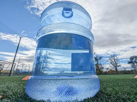 Large bottle, water container on the background of the sky and football field. Stock Photos