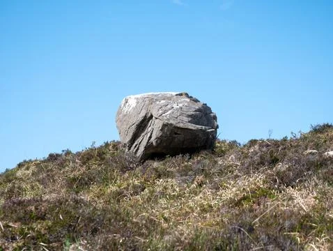 Large boulder on grassy hillside under blue sky Stock Photos