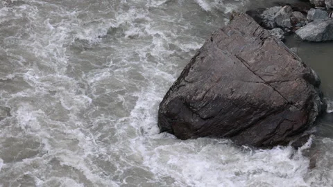 Large boulder standing in turbulent rushing mountain river water Видео 335308827