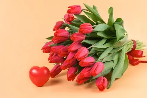 A large bouquet of red tulips and heart lie on a soft beige background - spri Stock Photos