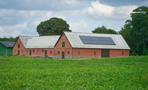 Large brick barn building with rooftop solar panels by green field. Stock Photos
