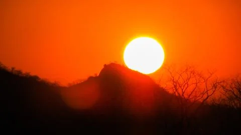 A large, bright sun creates a dramatic orange sky and silhouette of mountai.. Stock Photos