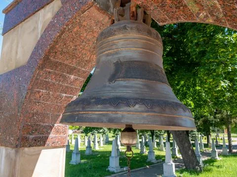 A large bronze bell under an arch in a Christian military cemetery. Stock Photos