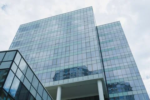 A large building features multiple glass windows that reflect the clouds and  Stock Photos