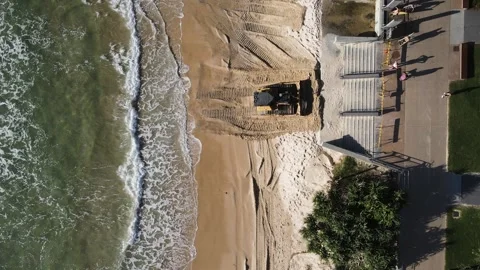 A large bulldozer pushes sand towards a concrete beach access area at a popular Stockbeeldmateriaal 307264129