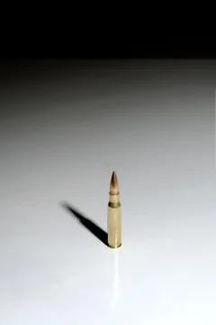 Large bullet standing on a white surface with long shadow Stock Photos