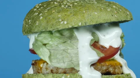 Large burger with meat patty and green bun, onion, tomato, melted cheese, salad Vídeo Stock 102918366