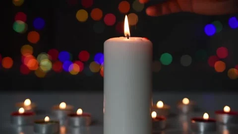 A large burning candle, standing in a dark room among other small candles. Stock Footage 148138995