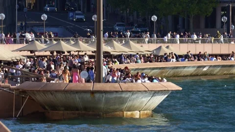 A large, bustling crowd of people enjoys drinks and dining at the sunlit Stock Footage 341503059