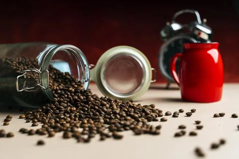 A large can of coffee beans is poured out of it. Near a glass and a clock Stock Photos