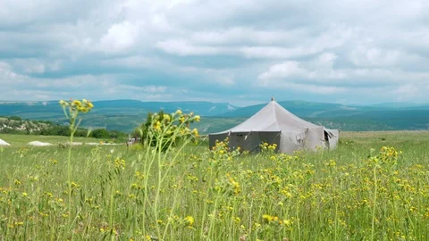 A large canvas tent stands in the middle of a field in the mountains. Stock Footage 114974772