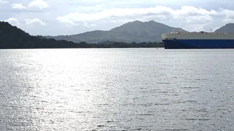 Large car carrier ship navigating calm tropical coastal waters with mountains Stock Footage 344972147