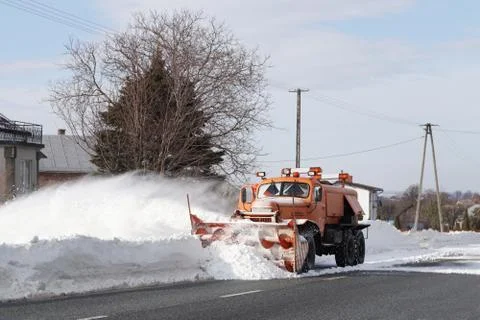A large car with a plow clears the road from snow. Orange cargo special equip Stock Photos