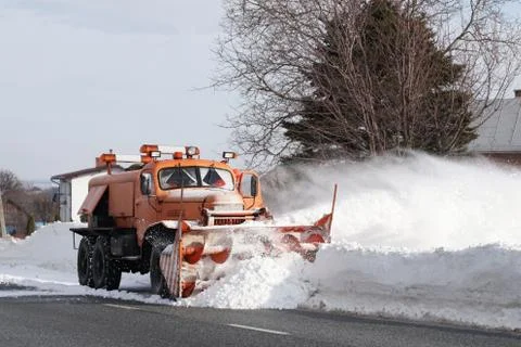 A large car with a plow clears the road from snow. Orange cargo special equip Stock Photos