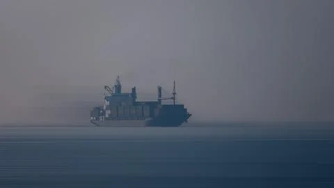 Large Cargo Container Ship Sailing Through Dense Coastal Morning Fog 库存照片