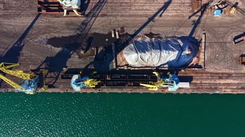 Large cargo cranes work on a dock to lift goods from a ship covered with a tarp Stock Footage 335381610