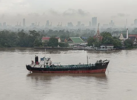 A large cargo ship on the Chao Phraya River with a city skyline and Wat Ban.. Stock Photos