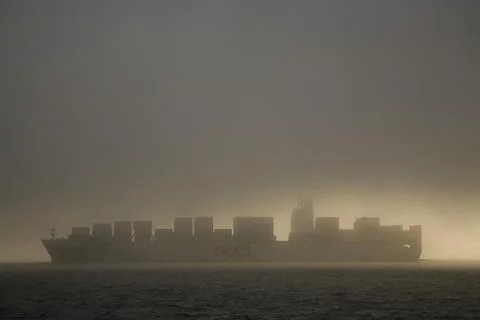 A large cargo ship cruises under a gray sky with light behind, Washington, USA. 写真素材