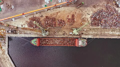 Large cargo ship at a dock loading scrap metal during daytime in a busy Stock Footage 341397824