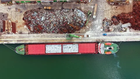 Large cargo ship loads scrap metal at a port while construction vehicles work Stock Footage 340930062