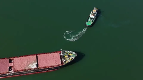Large cargo ship is moored while a tugboat approaches to assist in navigation at Stock Footage 331155011