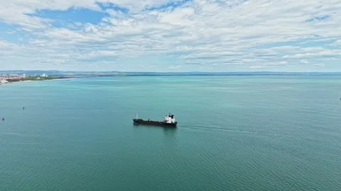 Large cargo ship moves across blue water under a cloudy sky near a coastal city Stock Footage 340174556