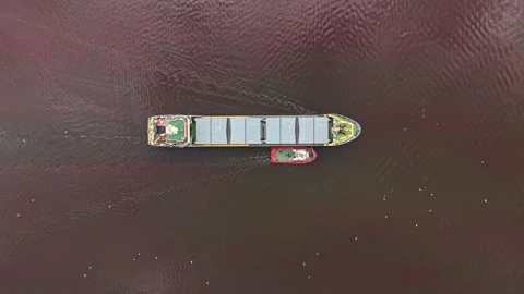 A large cargo ship is moving through water while a small tugboat assists near Stock Footage 341129204