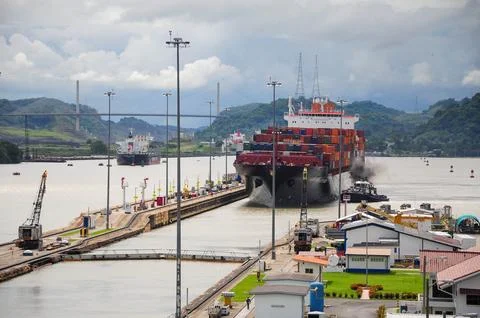A large cargo ship navigates through the Panama Canal locks under a cloudy sk Stock Photos