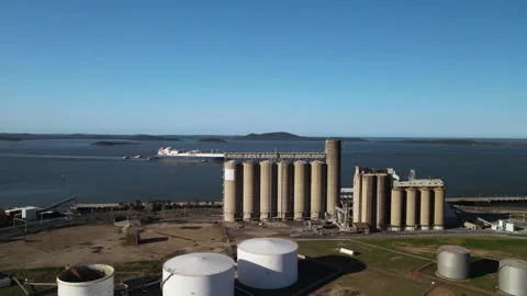 A large cargo ship navigates the waters of a industrial port near a towering Stock Footage 329099363