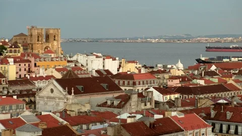 Large cargo ship passes behind the rooftops of central Lisbon at sunset. Stock Footage 119765176