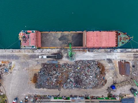 Large cargo ship at a port loading scrap metal from a pile on the dock whil.. Stock Photos