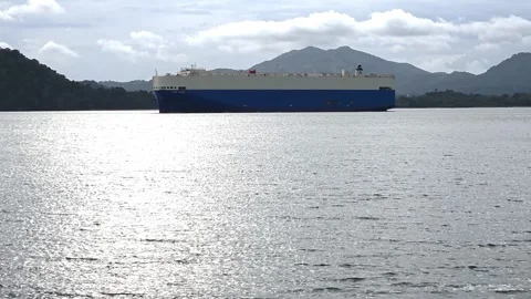Large cargo ship sailing across calm tropical waters with mountain background Stock Footage 344969715