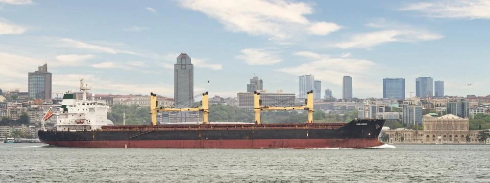 Large cargo ship sails through the Bosphorus Strait, dwarfed by the towering Stock Photos