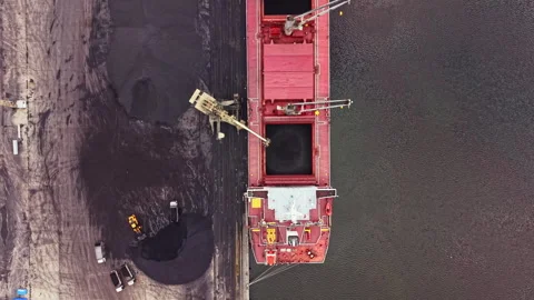 Large cargo ship is unloading coal at a shipping terminal in a busy port during 스톡 동영상 340883240