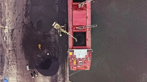 Large cargo ship unloading coal at a port with trucks and machinery nearby 스톡 동영상 341128209
