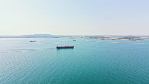 Large cargo ships navigate calm waters near the coast in a clear blue sky above Stock Footage 340941122