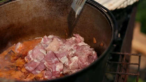 In large cast iron pot preparing dish, red with meat onions and other components 库存影片 115451844