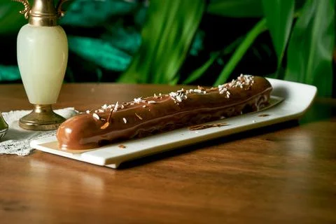 Large chocolate eclair with coconut and chocolate chips on wood background Stock Photos