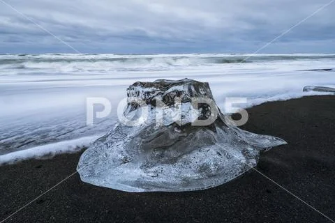 Large chunk of ice sitting on the shore of Iceland with dramatic skies in behind Stock Photos