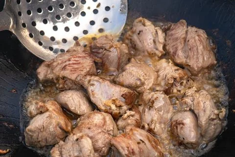 Large chunks of lamb sheep fried in oil with bubbles in a black cauldron cl.. Stock Photos