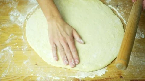 Large circle of dough on yellowish board. Cook's hand runs over rolling dough Stock Footage 220683773